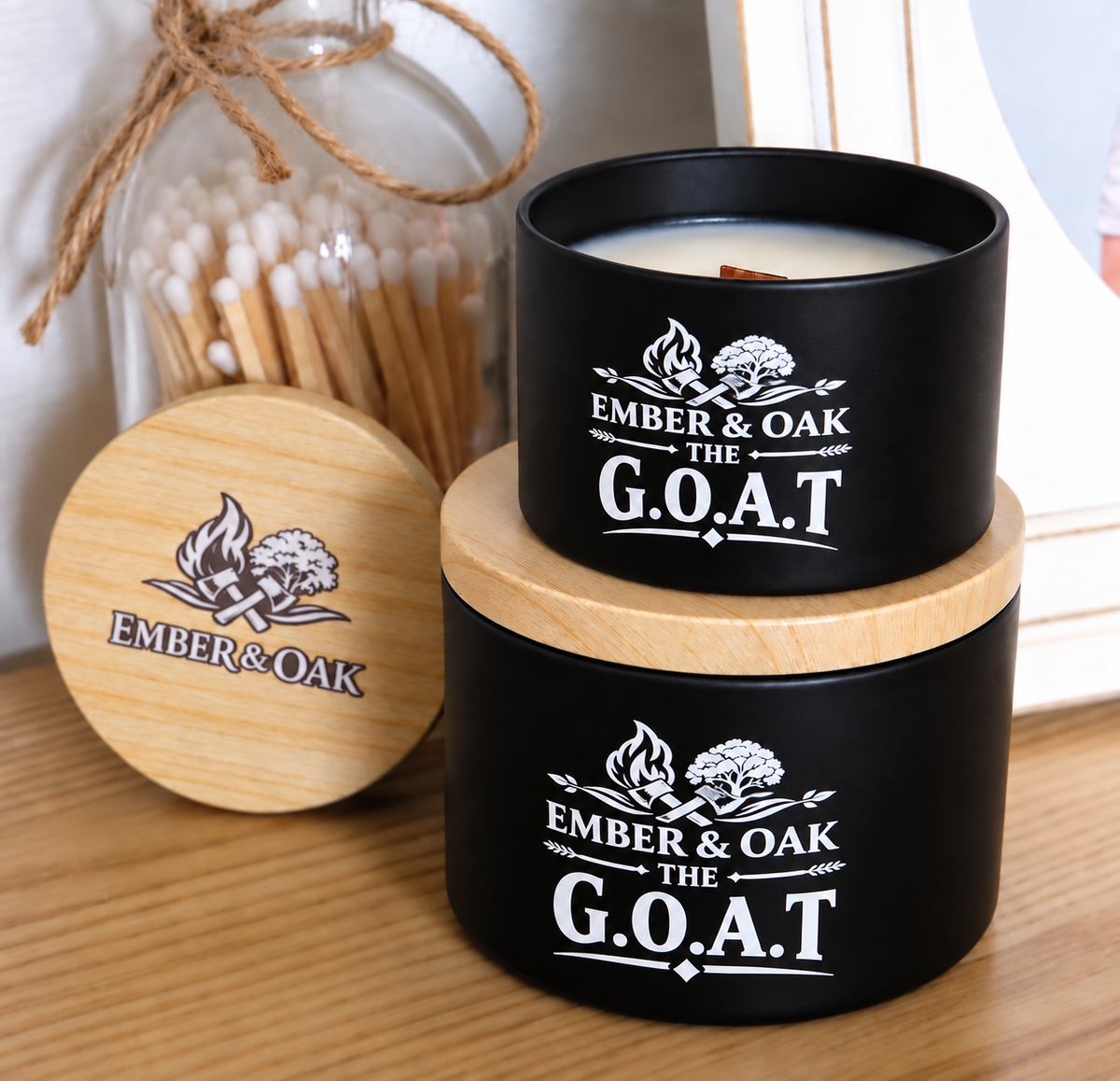     The G.O.A.T luxury candle with wooden lid displayed alongside Ember & Oak packaging and accessories