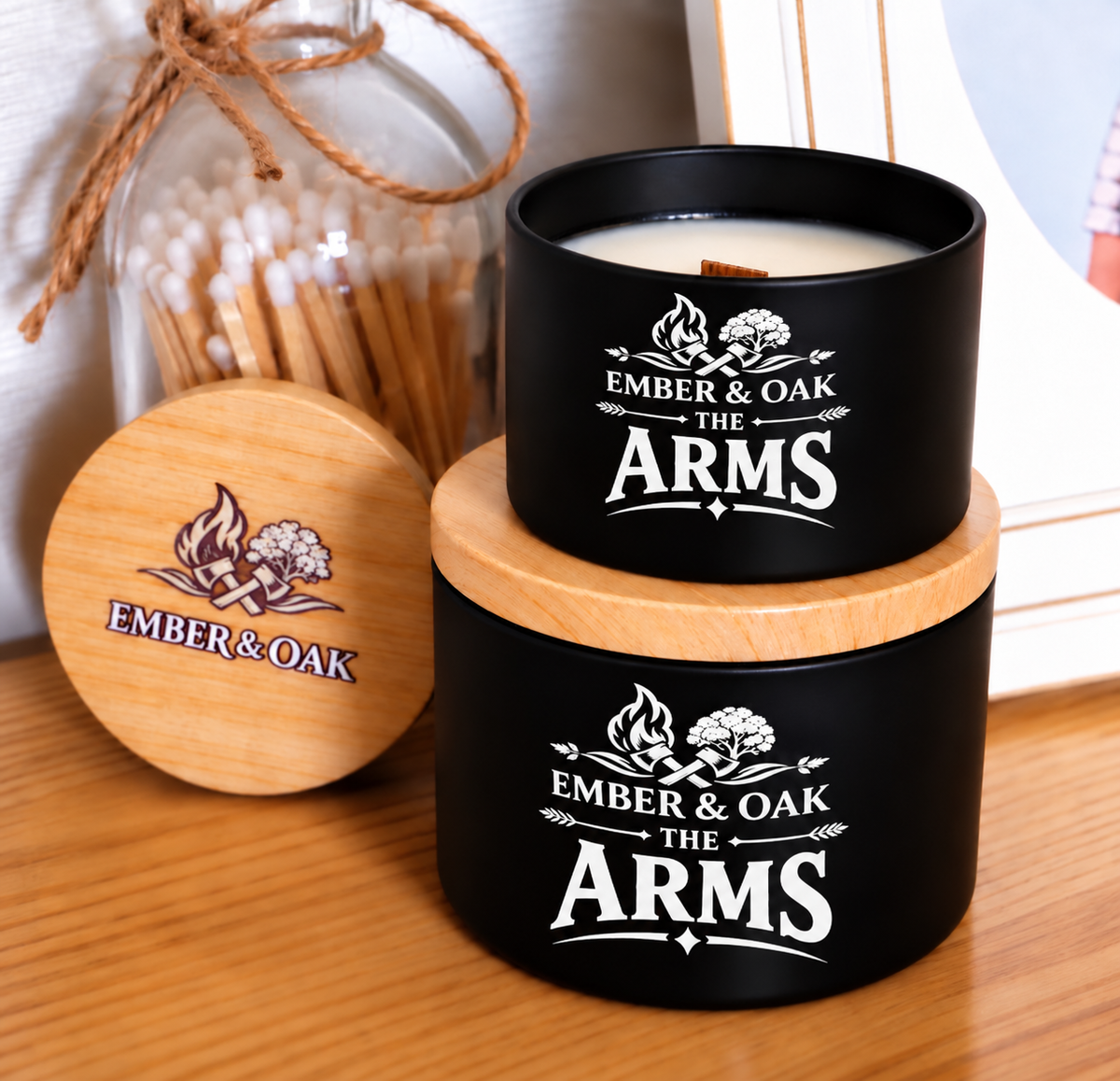     The Arms luxury candle with wooden lid displayed alongside Ember & Oak packaging and accessories